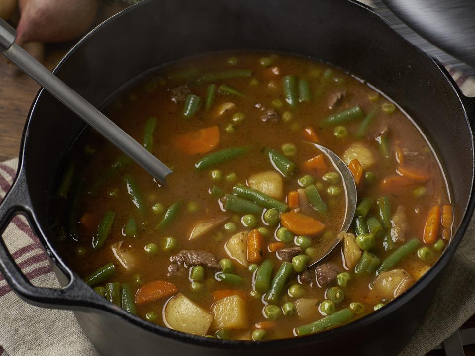 close up view of Beef and Vegetable Soup with carrots, potatoes and green beans in a pot with a ladle