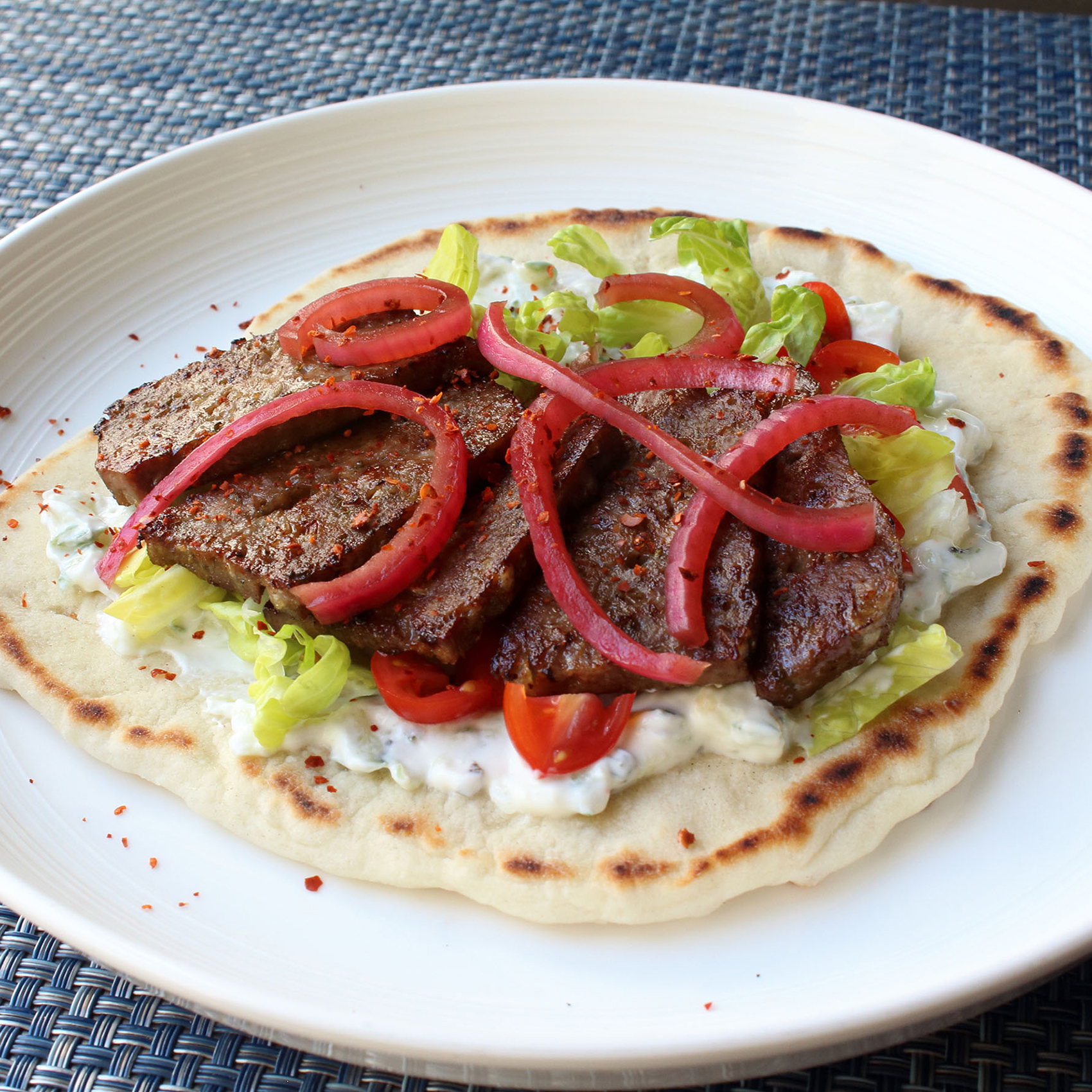 close up view of an American Gyros with red onions, lettuce, and tomatoes on a pita on a plate