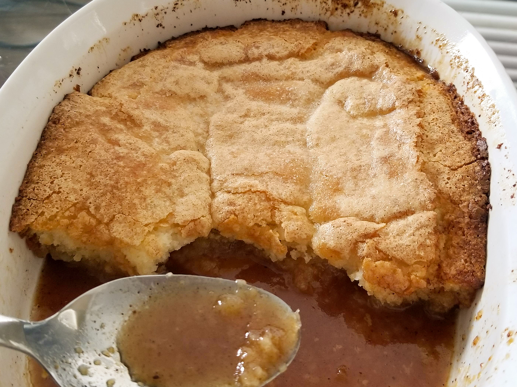 close up view of Peach Cobbler in a white baking dish with a serving spoon