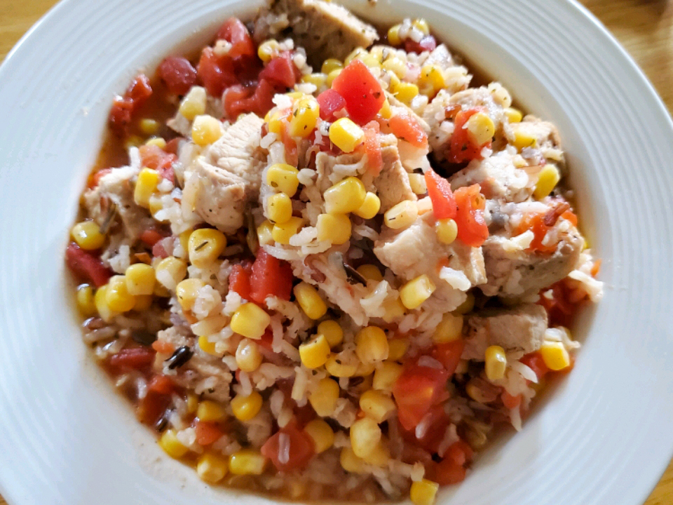 close up view of a Pork Chop Skillet with corn, tomatoes, and rice in a white bowl