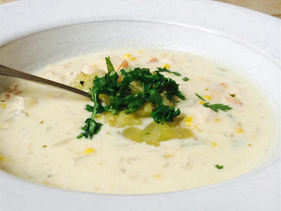 close up view of Mexican Chicken Corn Chowder garnished with fresh herbs in a white bowl with a spoon