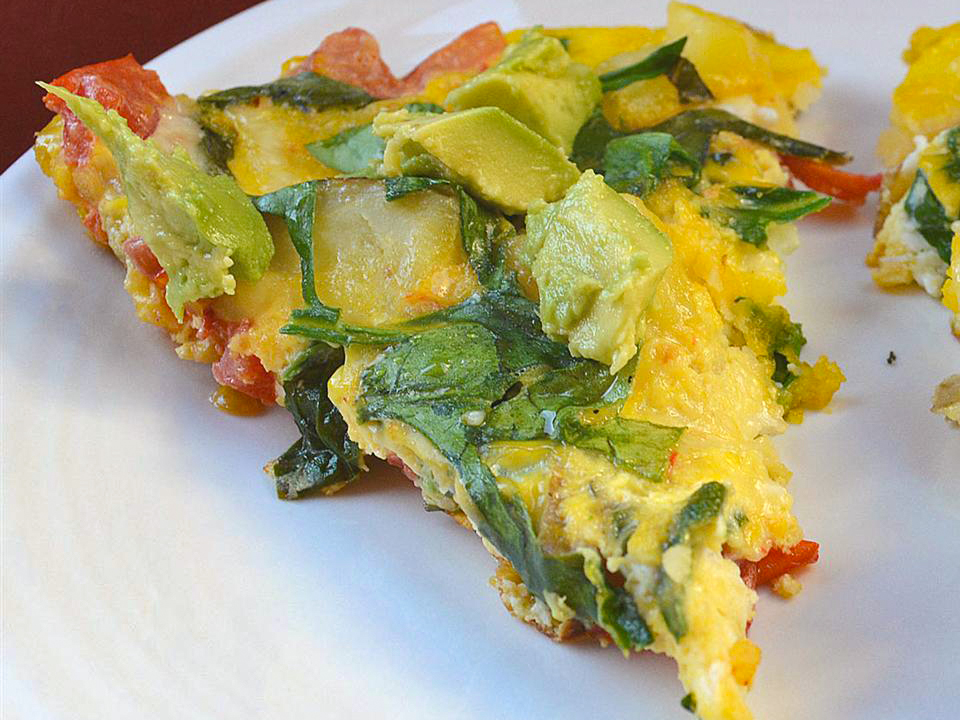 close up view of a slice of an American Frittata with spinach and avocado, on a white plate