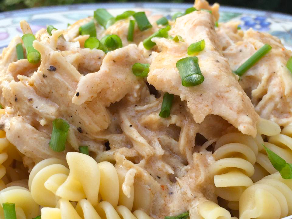 close up view of Slow Cooker Chicken over pasta, garnished with green onions in a bowl