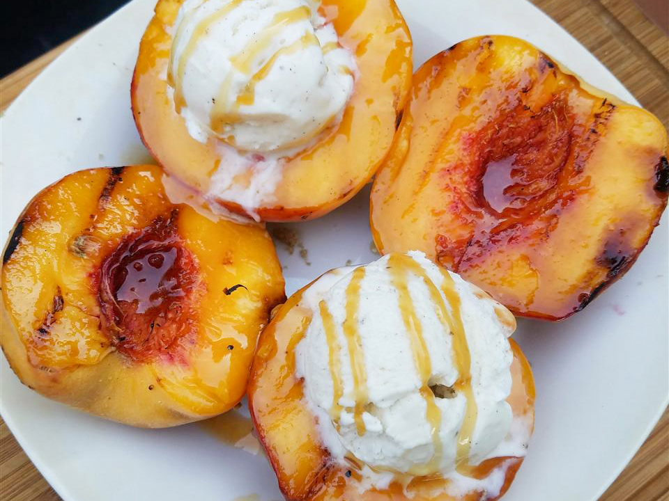 close up view of Grilled Peaches and Ice Cream garnished with honey on a white plate