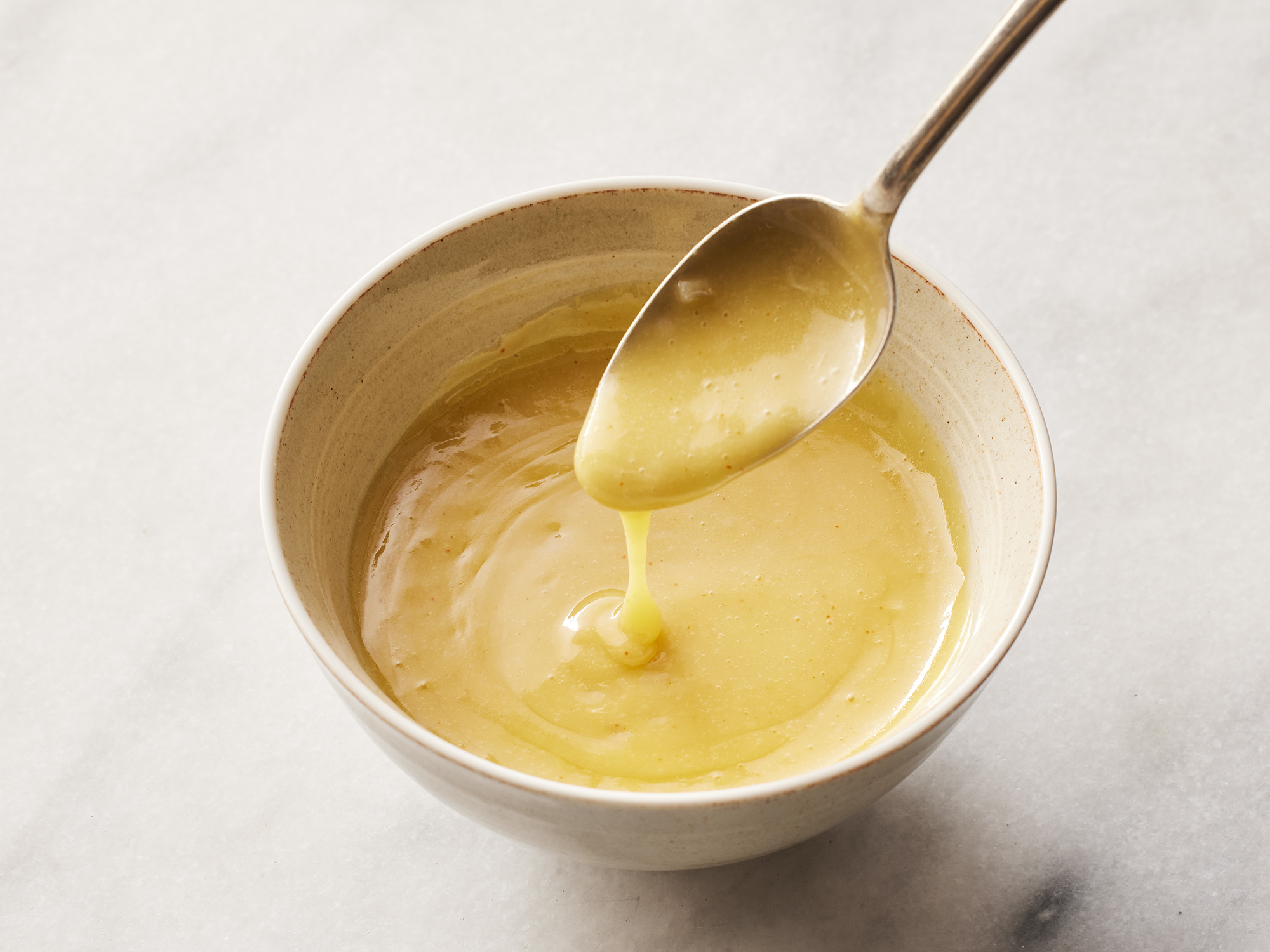 close up on a bowl of beurre blanc with a spoonful dripping down into the bowl