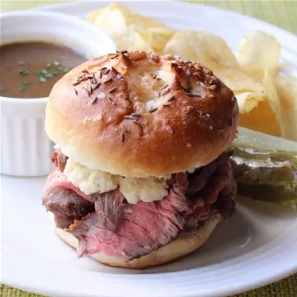 close up view of a Beef on Weck Sandwich served with potato chips and gravy on a white plate