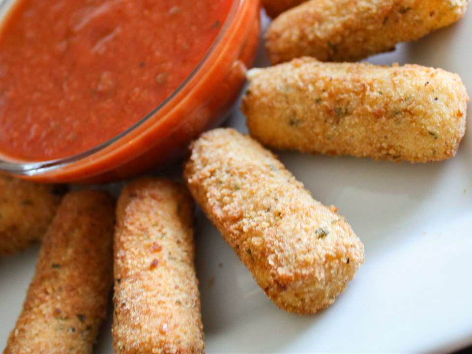 close up view of Fried Cheese Sticks served with red sauce in a glass bowl on a white plate
