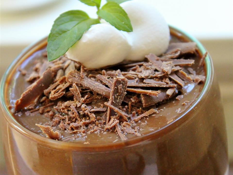close up view of chocolate pudding garnished with shaved chocolate and cream, garnished with herbs in a glass