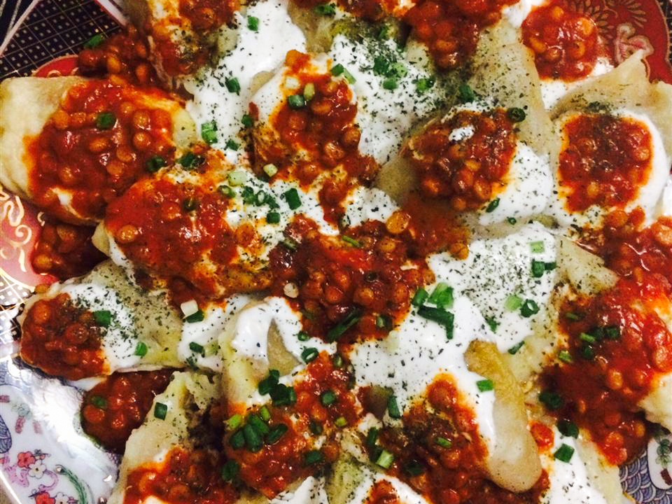 close up view of Afghan Beef Raviolis garnished with red sauce, yogurt and fresh herbs on a colorful plate