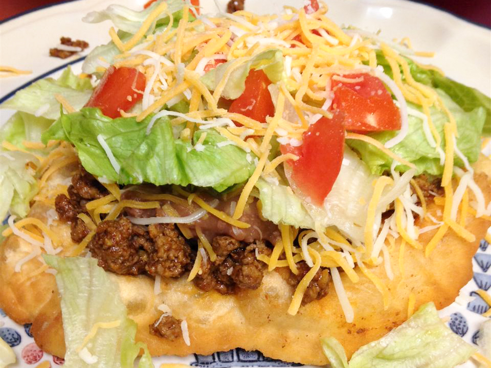 close up view of Fry Bread Tacos garnished with lettuce, tomatoes and cheese on a plate