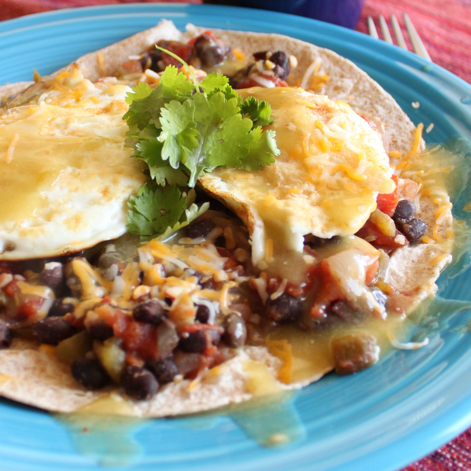 close up view of Black Bean Huevos Rancheros on a tortilla, garnished with fresh herbs, on a blue plate