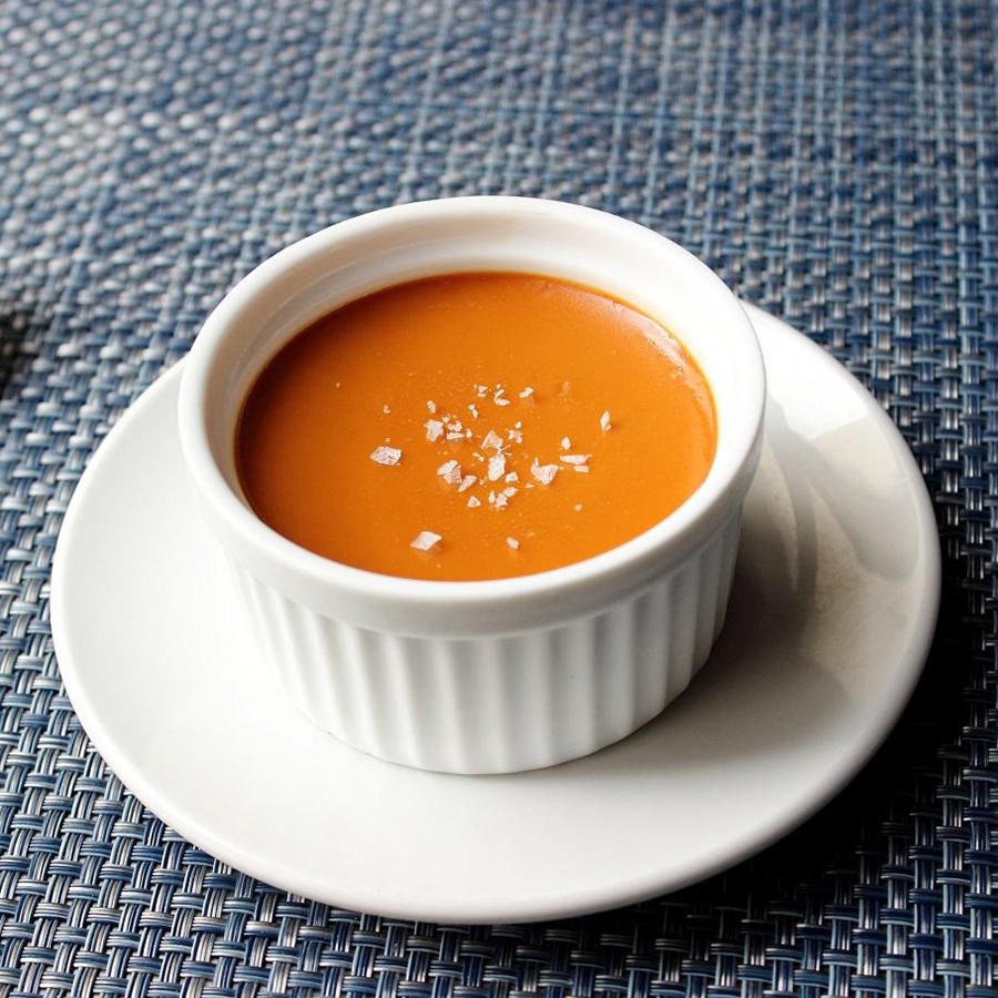 close up view of Salted Caramel Custard garnished with sea salt, in a white ramekin on a white plate