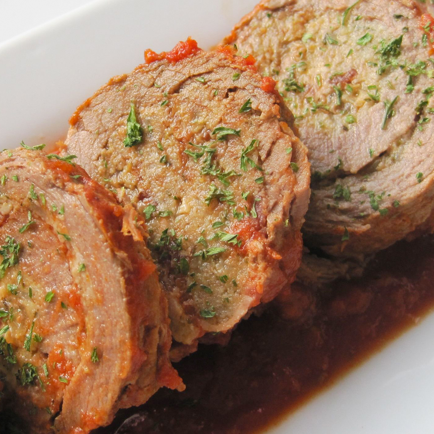 close up view of sliced Slow Cooker Braciole, garnished with herbs on a white platter