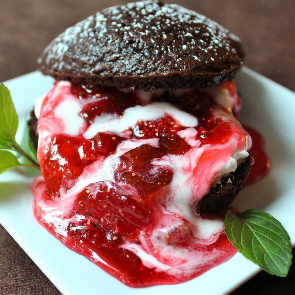 close up view of a chocolate cake sandwich with ice cream with Fresh Strawberry Sauce, garnished with mint, on a white plate