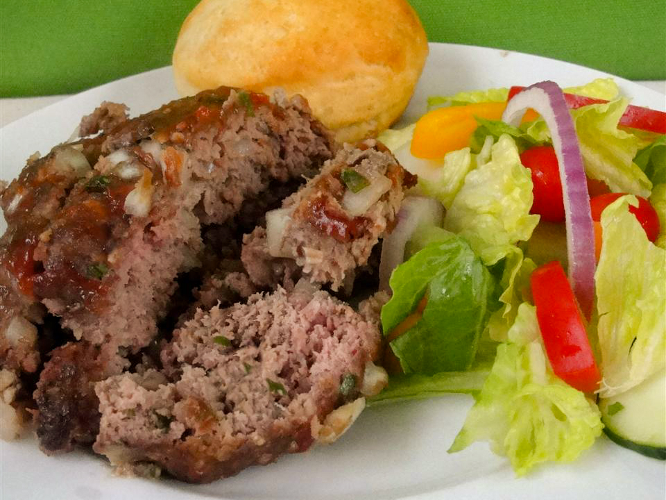 close up view of slices of Meatloaf served with salad and a biscuit on a white plate