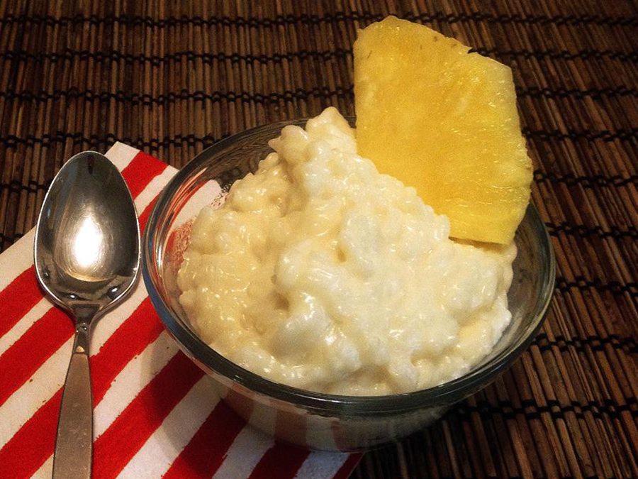 close up view of Creamy Coconut Rice Pudding garnished with a slice of pineapple in a glass bowl, next to a spoon