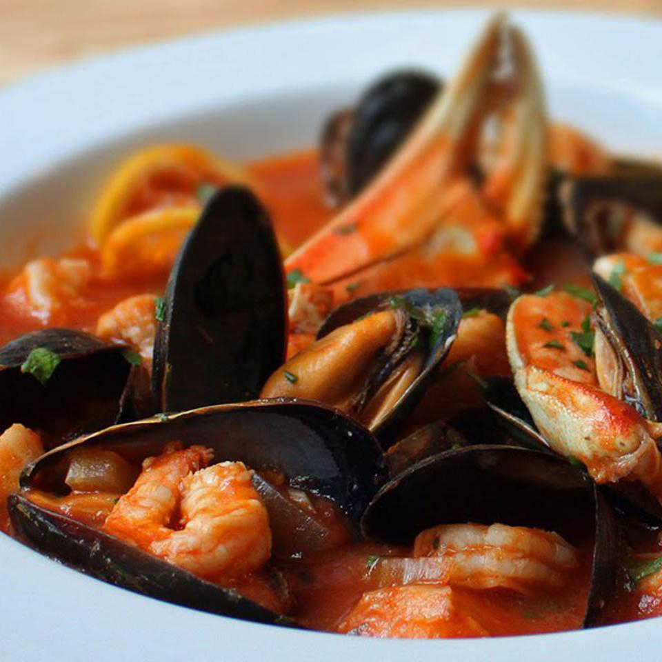 close up view of Cioppino with muscles, shrimp and crab claws in a white bowl