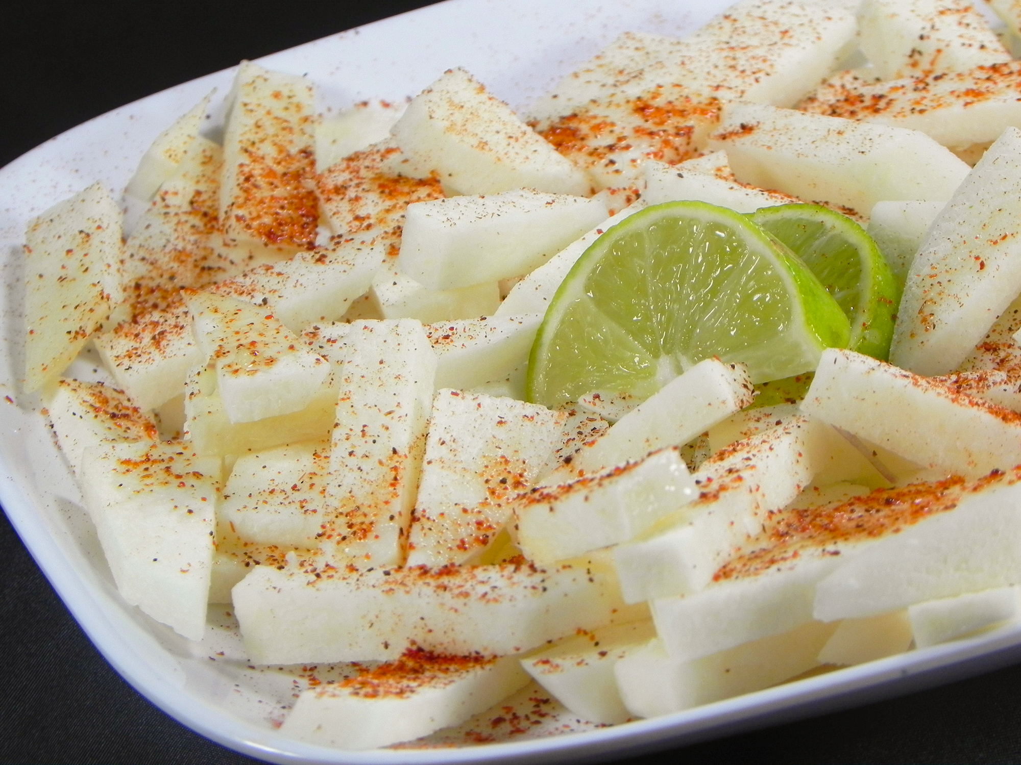 close up view of a Jicama Appetizer with jicama slices with seasoning and lime slices on a white plate