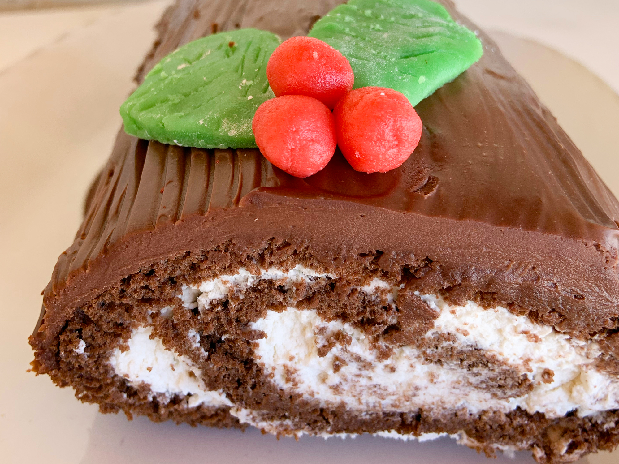 close up view of a Classic Yule Log cake with a white filling, garnished with brown icing and green and red marzipan