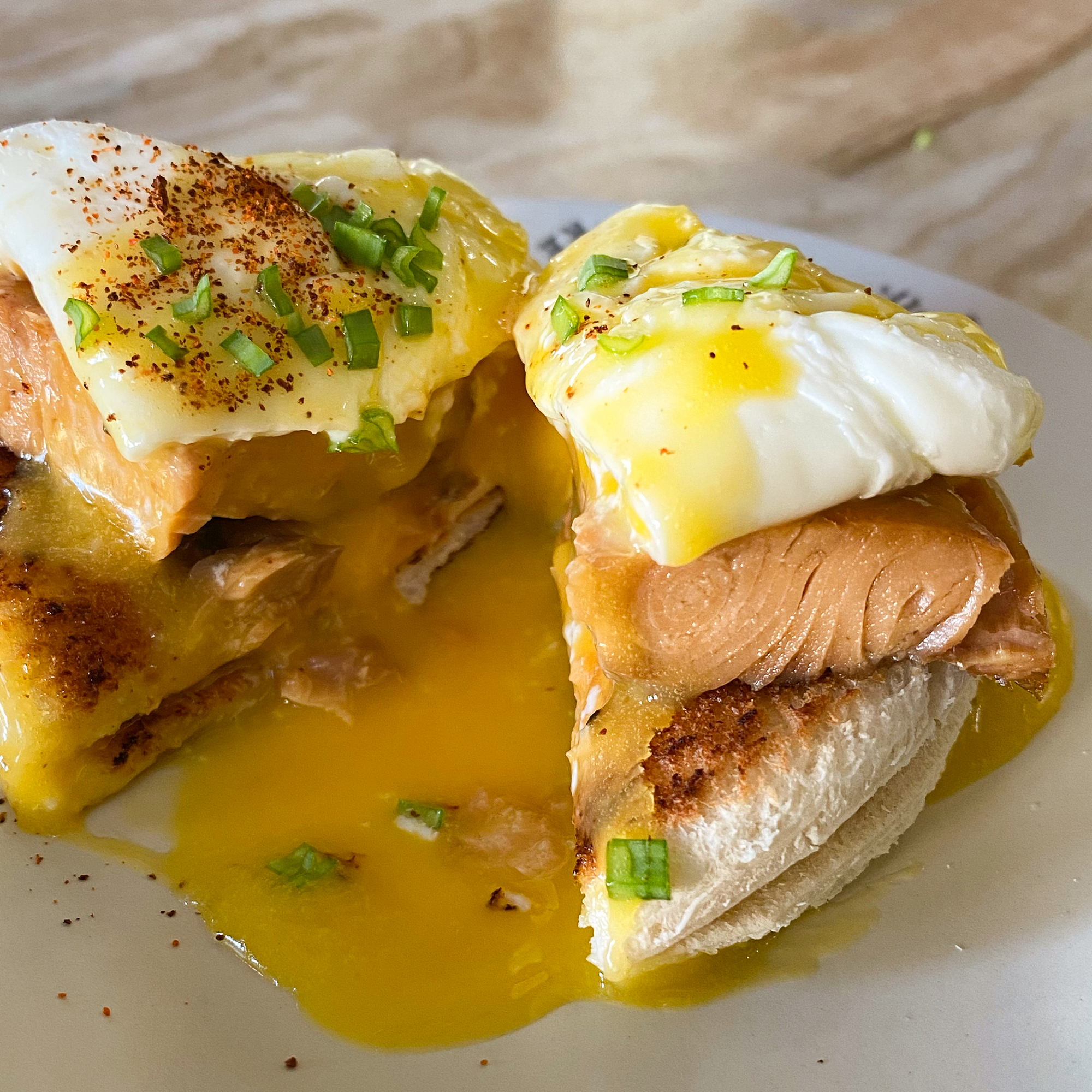 close up view of an Eggs Benedict with a Salmon fillet, garnished with green onions on a white plate