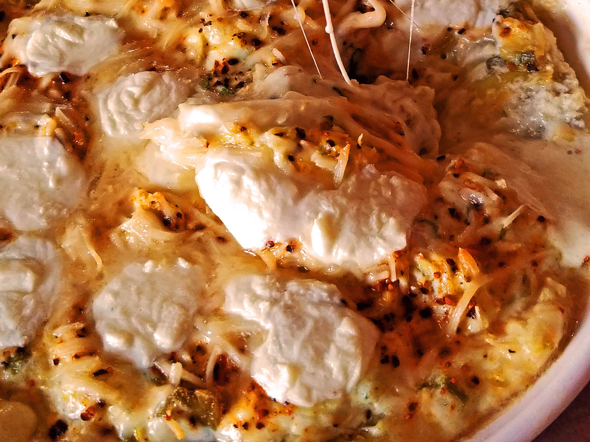 close up view of Artichoke Dip with melted cheese on top, in a white baking dish