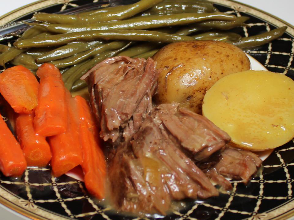 close up view of Pot Roast served with carrots potatoes and green beans on a plate