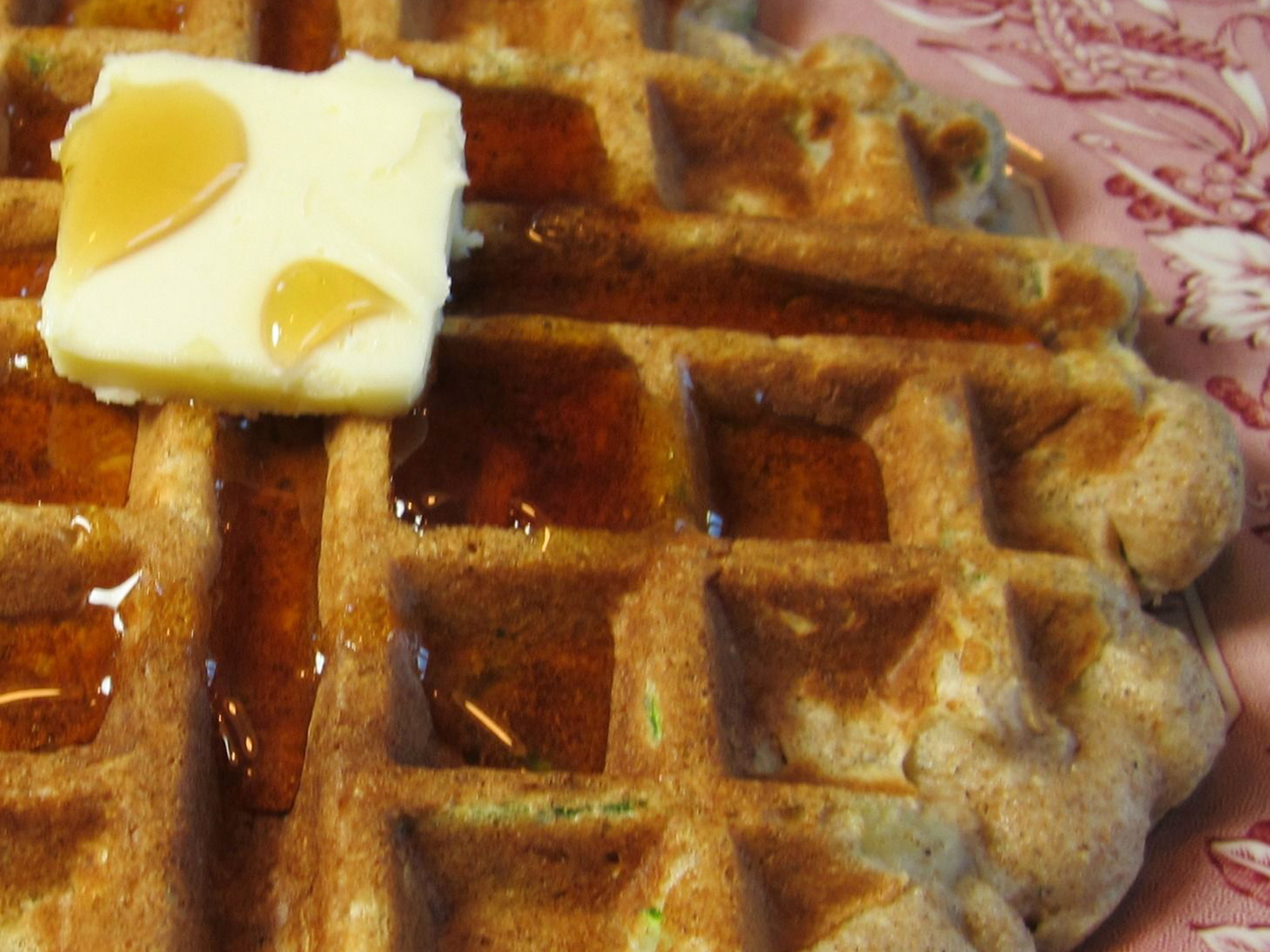 close up view of a Zucchini Oatmeal Waffle with syrup and butte on a pink plate
