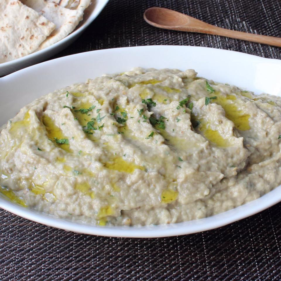 close up view of Baba Ghanoush garnished with oil and fresh herbs in a white bowl