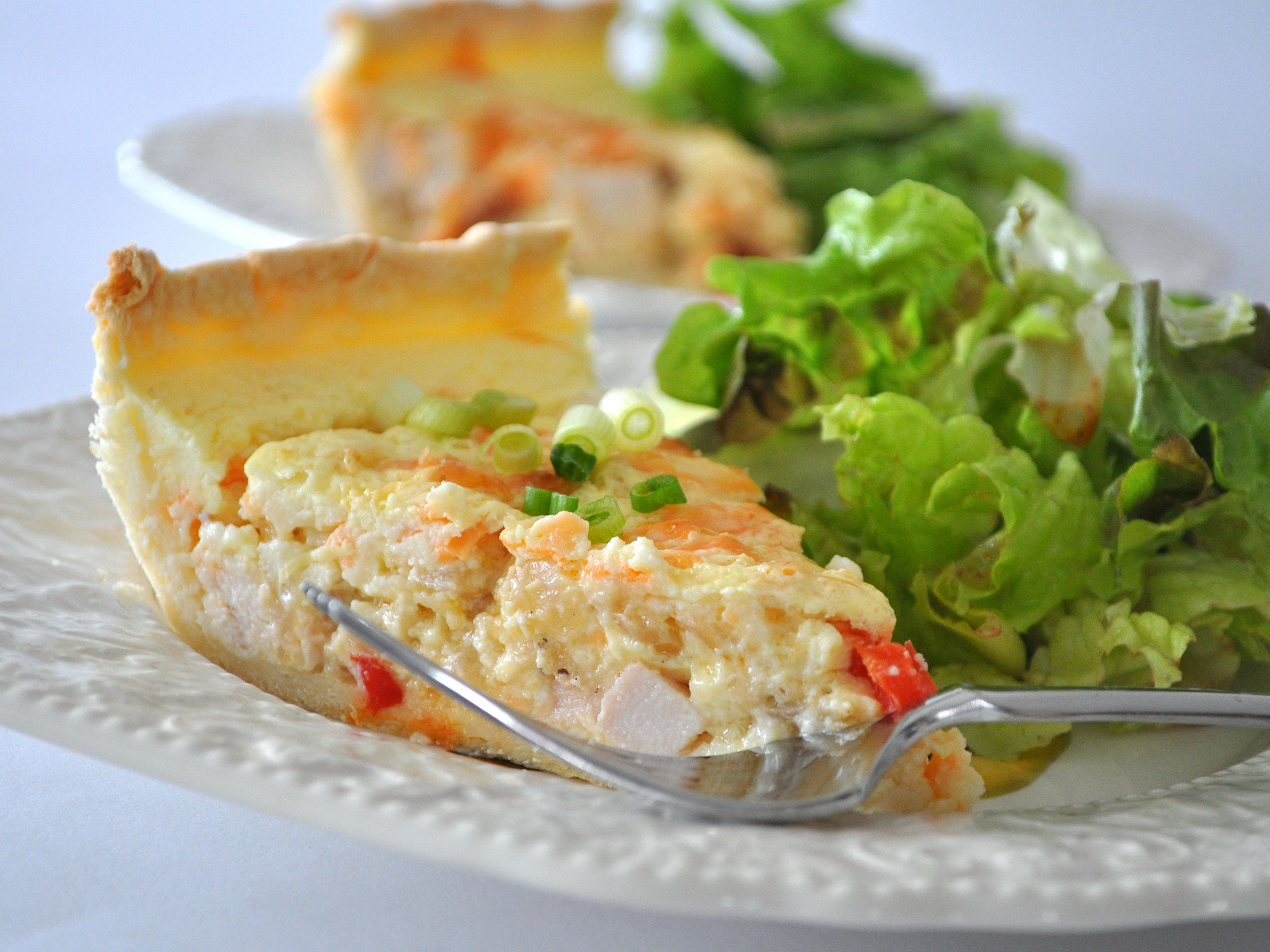 close up view of a slice of Sour Cream Chicken Quiche on plates with salad and a forks