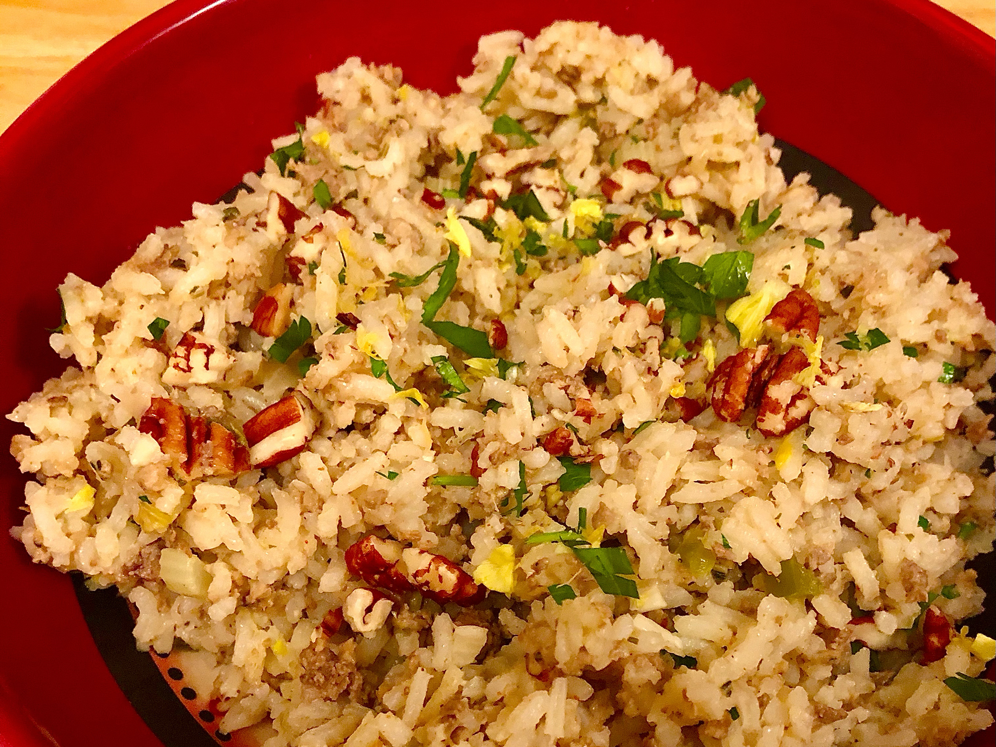 close up view of Southern Dirty Rice garnished with fresh herbs and nuts, in a red bowl