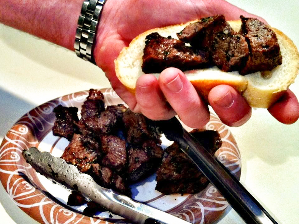 close up view of New York Spiedies, meat on a paper plate with tongs and meat on a bun held by a hand