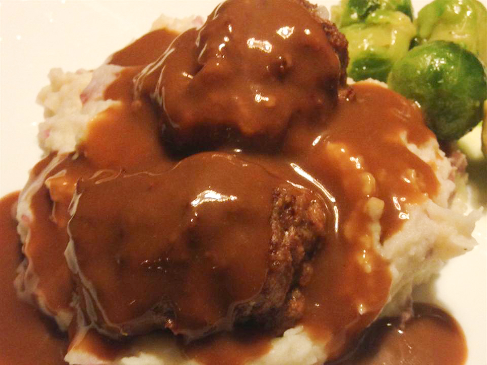 close up view of Baked Meatballs with gravy, over mashed potatoes, served with Brussels sprouts on a plate