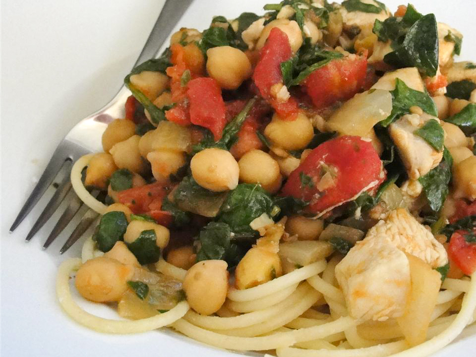 close up view of Pasta with Spinach, Chickpeas and tomatoes on a white plate with a fork