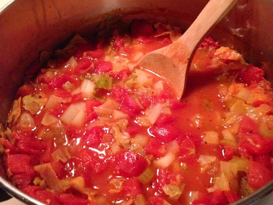 close up view of Cabbage, Potato, and Tomato Soup in a pot with a wooden spoon