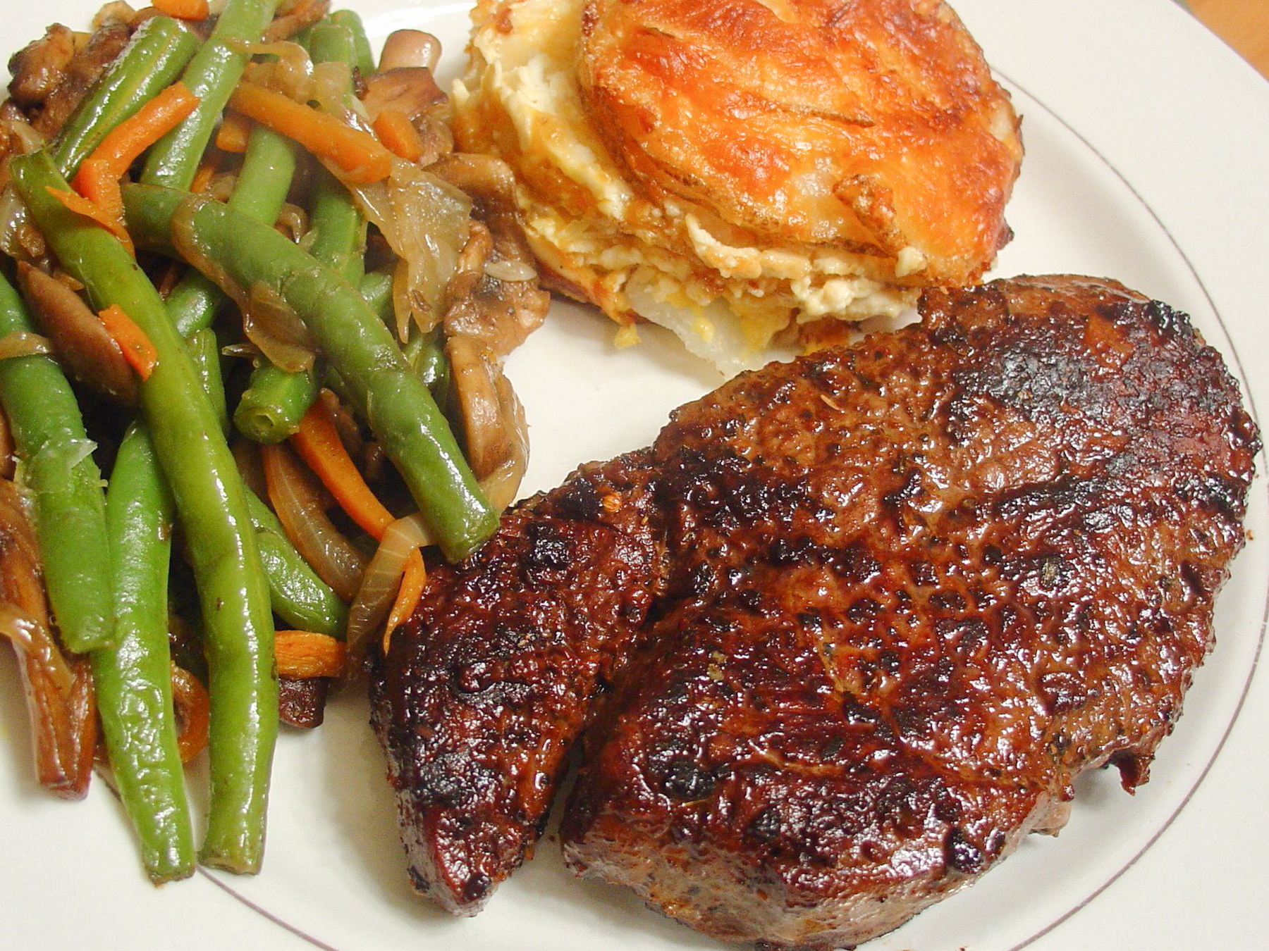 close up view of BBQ NY Strip served with green beans and carrots and potato gratin