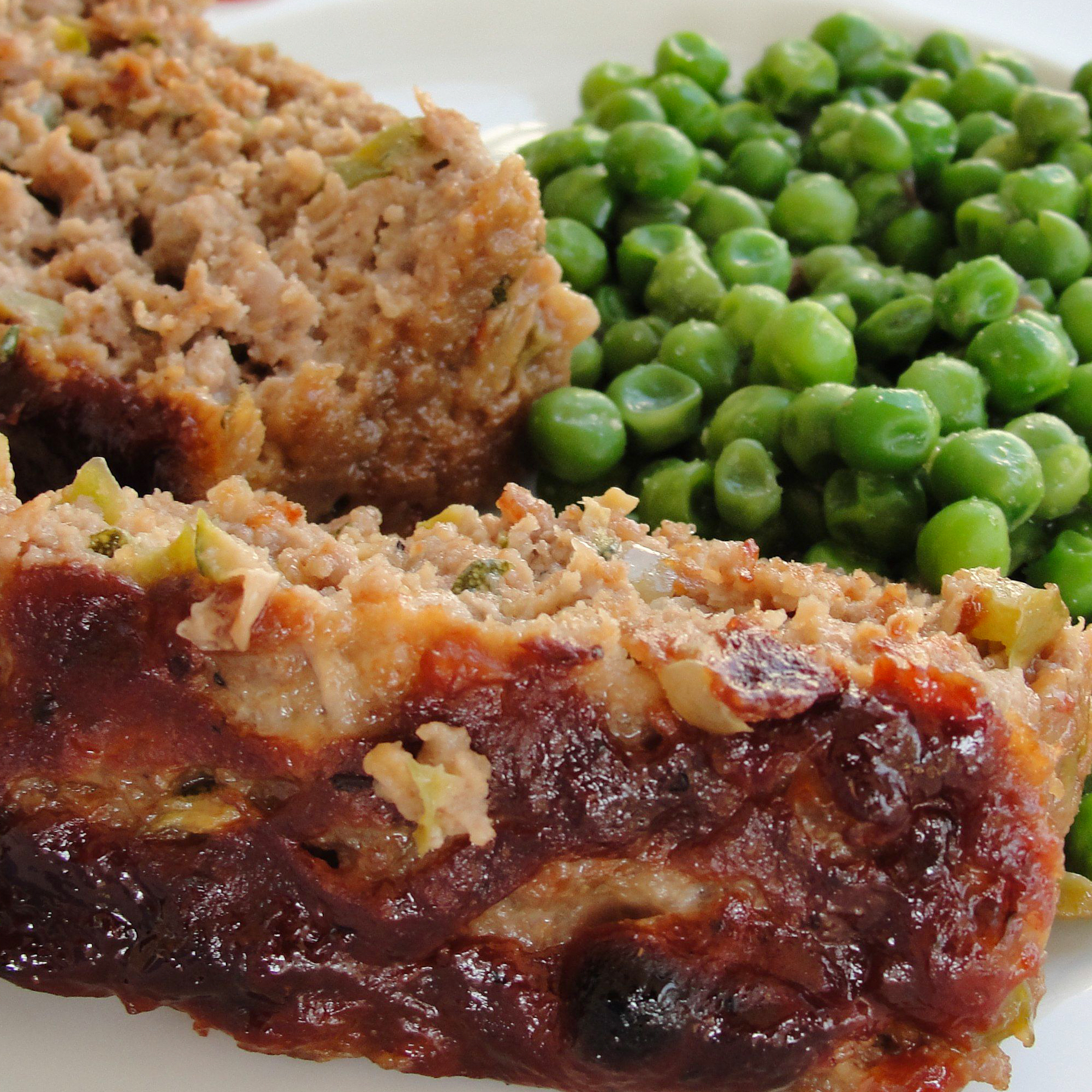 close up view of slices of Zucchini Ranch Meatloaf, served with green peas on a plate