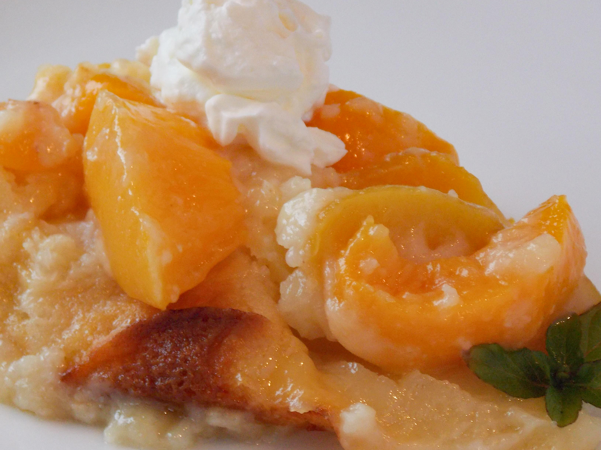 close up view of a slice of Quick Peach Cobbler topped with peaches and cream on a white plate