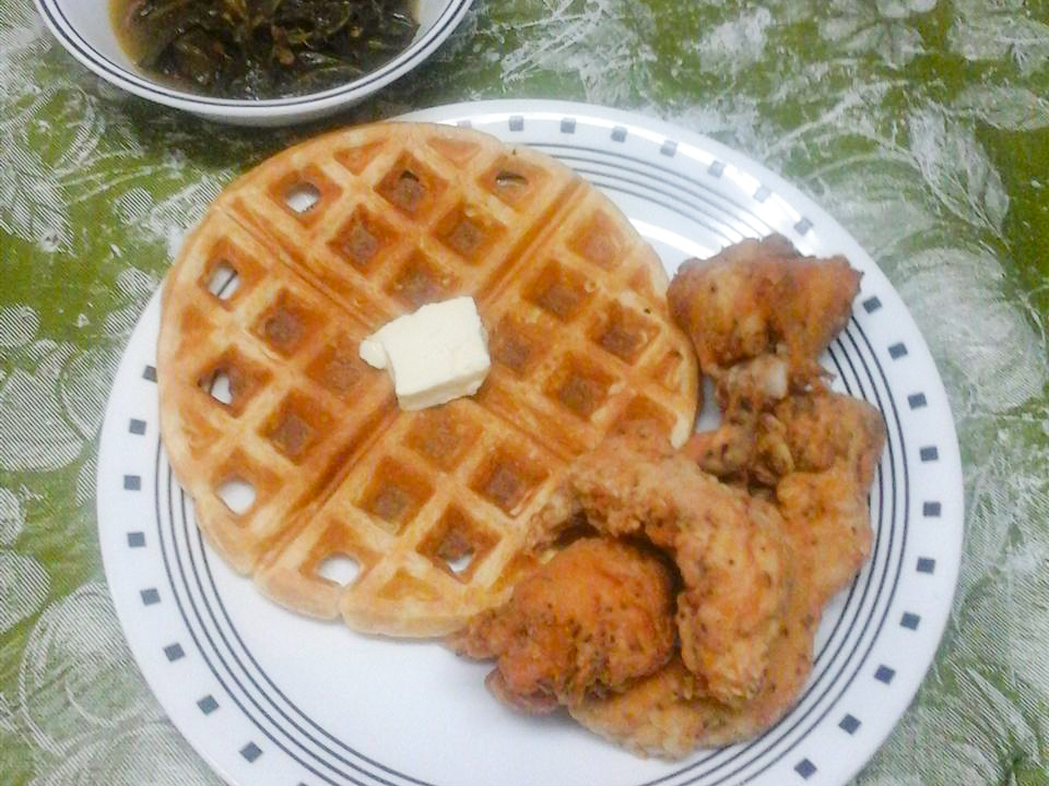 close up view of Waffle Iron Cornbread garnished with butter, served with fried chicken on a plate, next to collared greens in a bowl