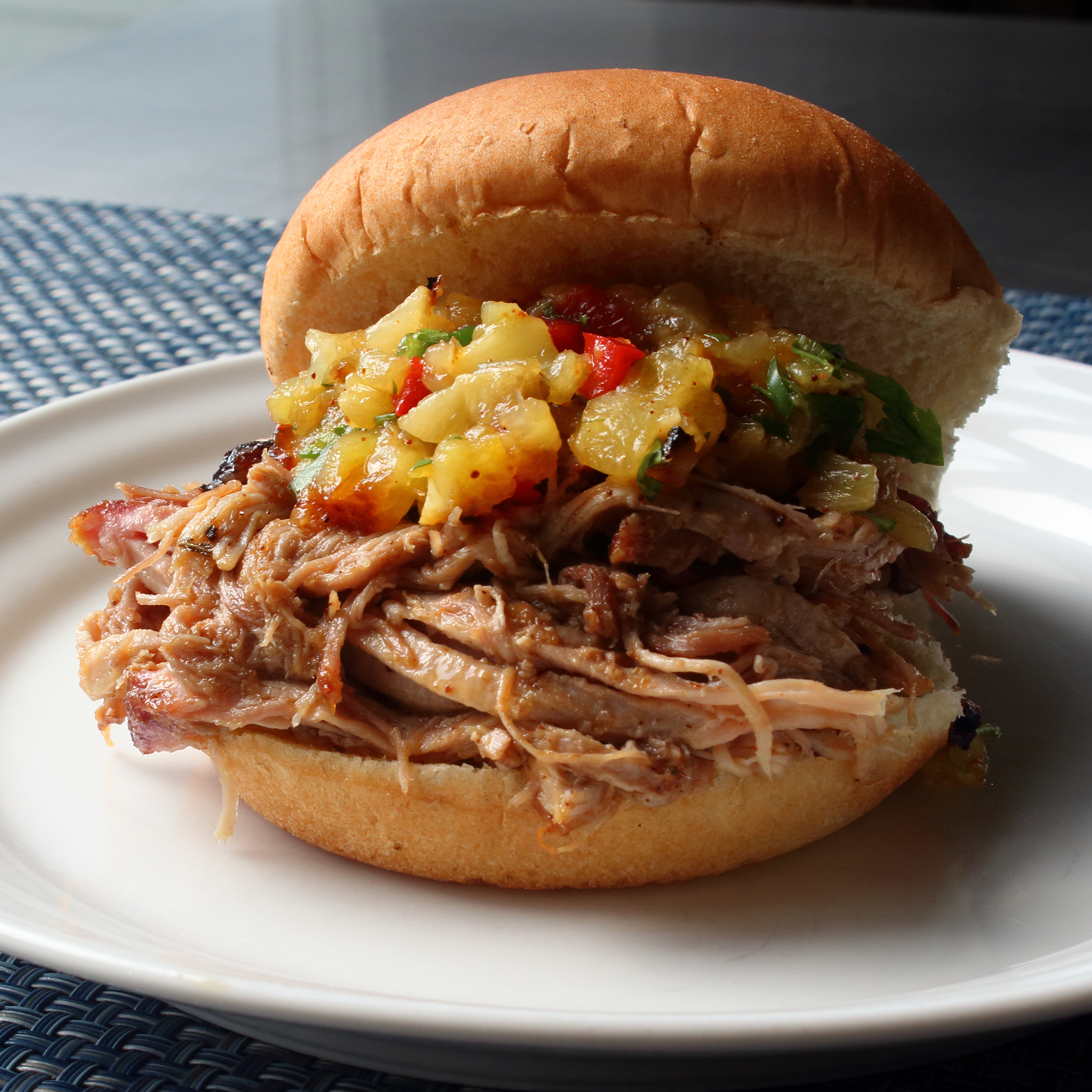 close up view of Pineapple Pulled Pork Al Pastor with pineapple relish on a bun, on a white plate