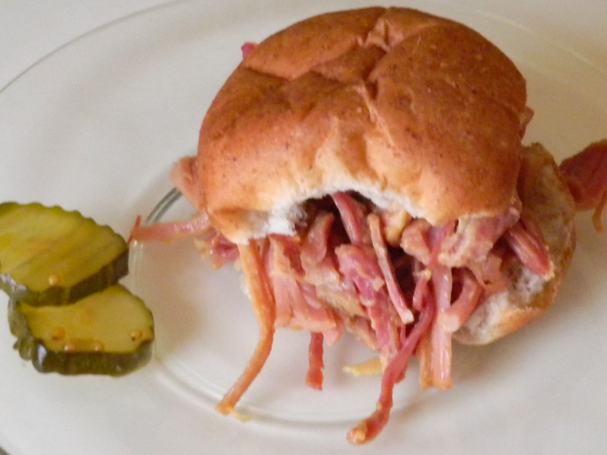 close up view of a Ham Sandwich and two pickle slices on a plate