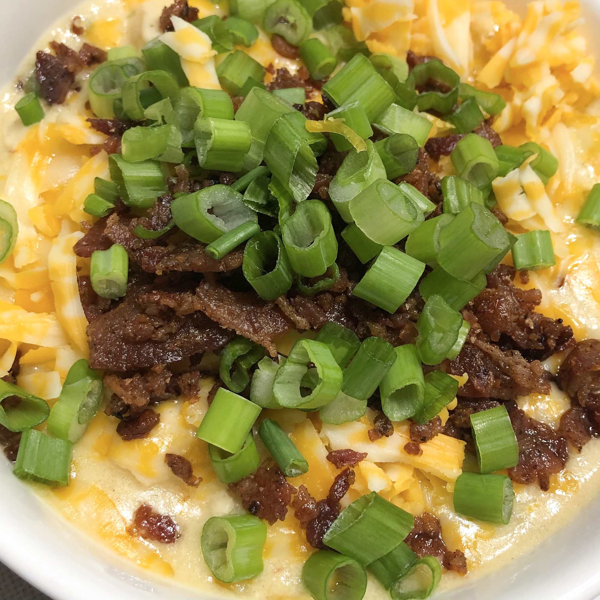 close up view of Loaded Chicken Potato Soup garnished with meat, cheese and green onions in a bowl