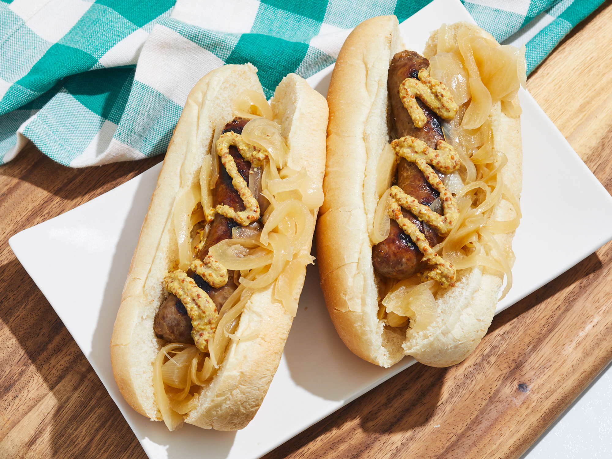 looking at two Wisconsin bratwurst on a plate, topped with onions and mustard