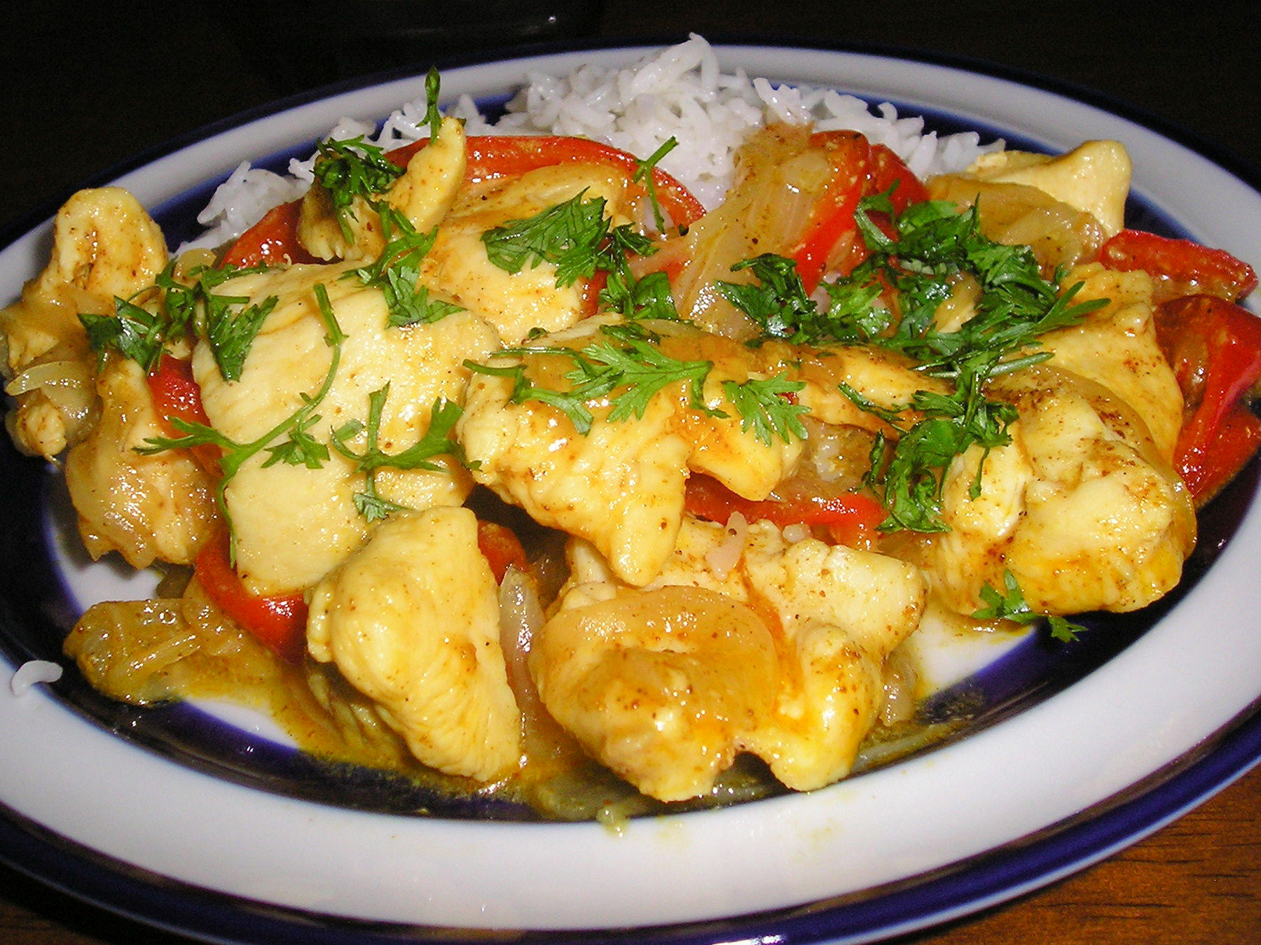 close up view of Maple-Curry Chicken with red peppers garnished with fresh herbs, over white rice on a plate