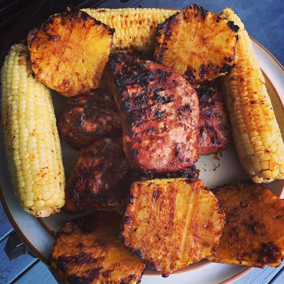 close up view of a pile of Grilled Mongolian Pork Chops with grilled pineapple pieces and corn on a platter