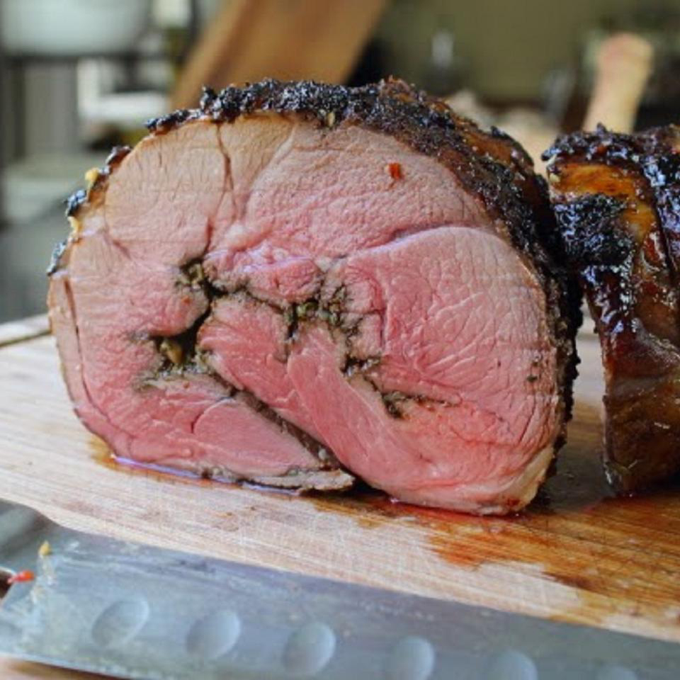close up view of a sliced Roasted Leg of Lamb on a wooden cutting board, next to a knife