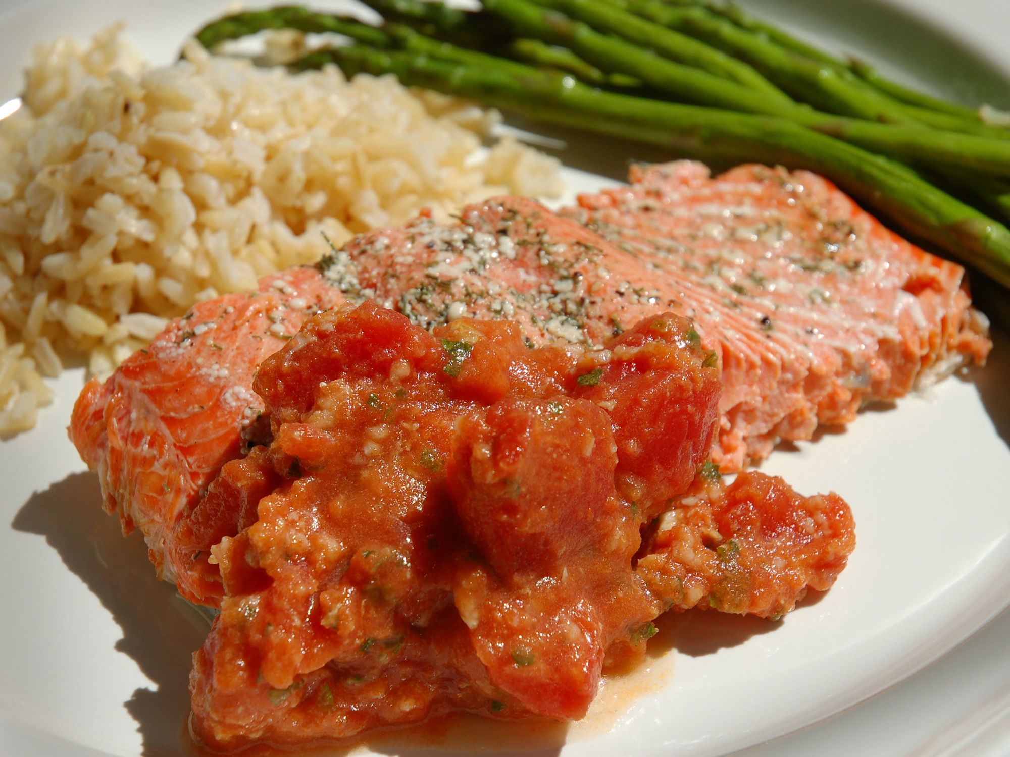 close up view of Salmon with Tomatoes with seasoning, served with rice and asparagus on a white plate