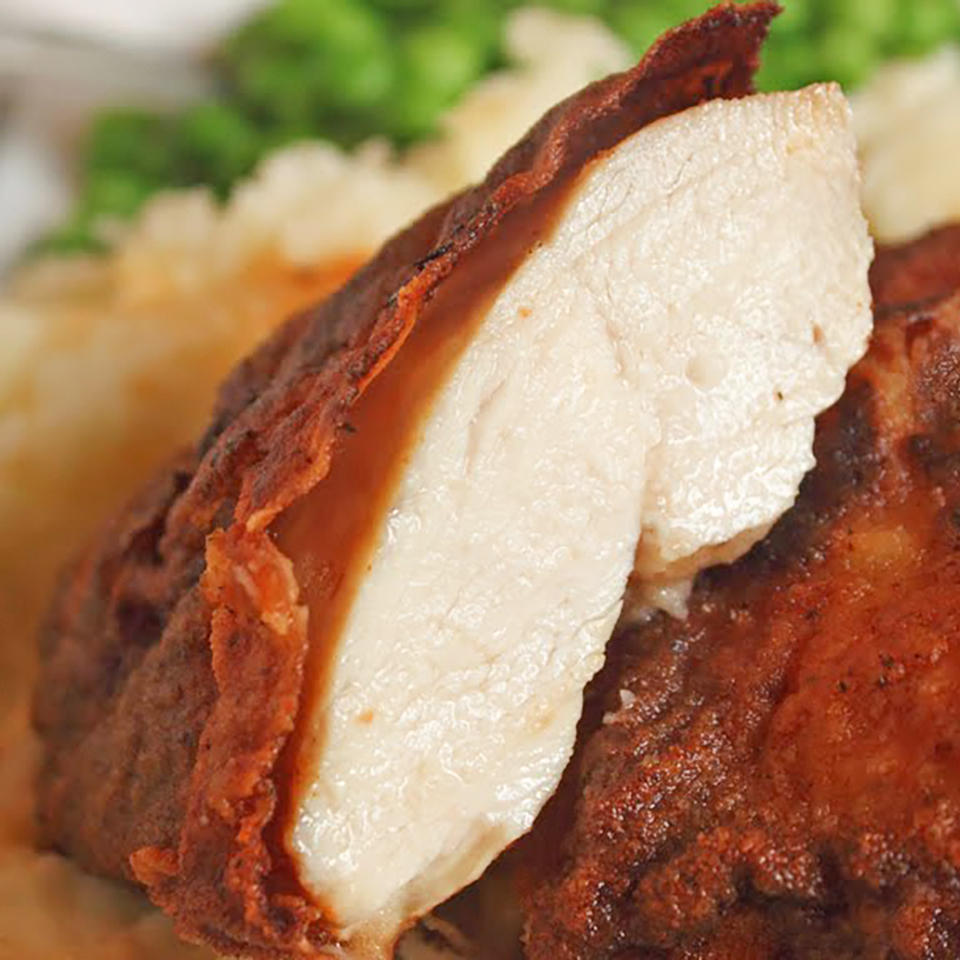 close up view of sliced Honey-Brined Fried Chicken Breasts served with mashed potatoes and peas on a plate