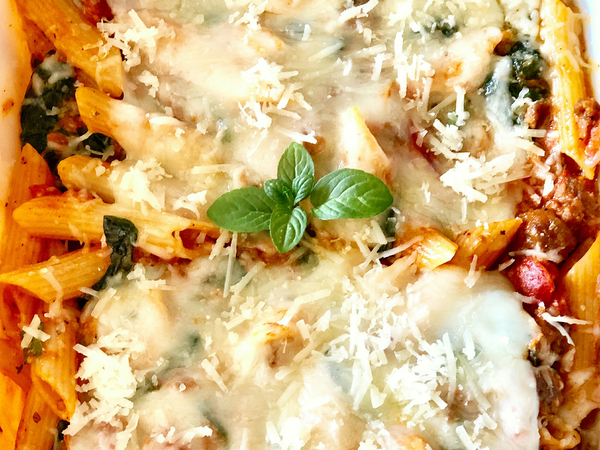 close up view of Three-Cheese Chicken Penne Pasta Bake garnished with cheese and fresh basil