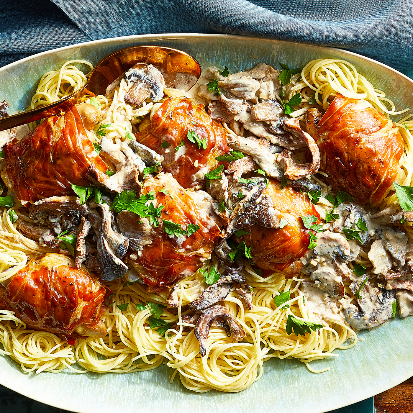 close up view of Chicken with Mushrooms, Prosciutto, and Cream Sauce, garnished with fresh herbs, served over pasta on a platter with a serving spoon