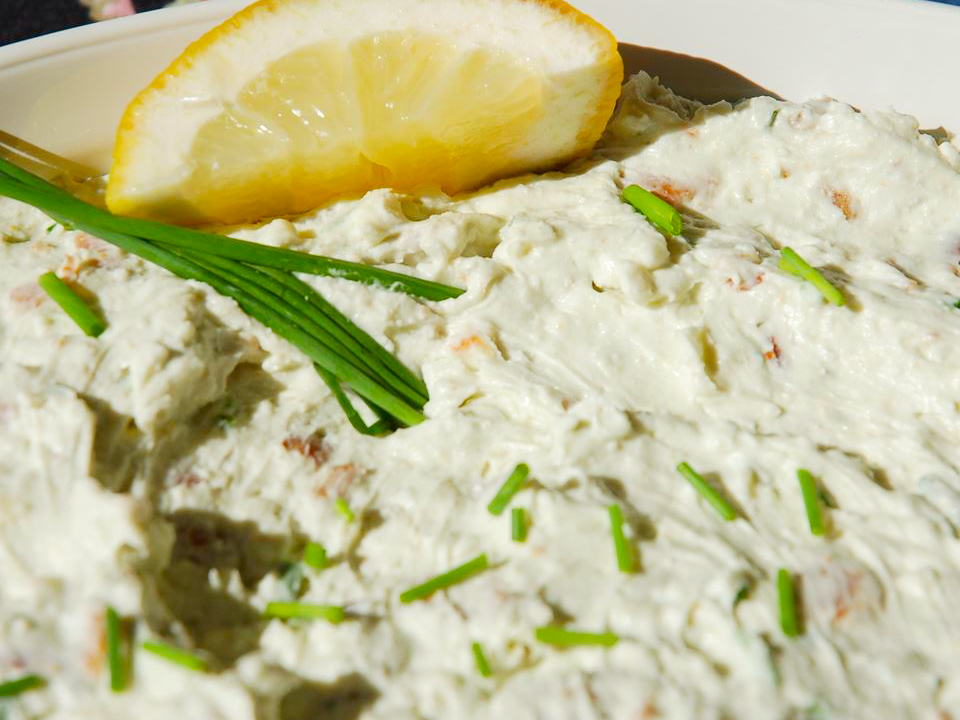 close up view of Warm Blue Cheese Dip with Garlic and Bacon, garnished with chives and a lemon slice, in a white bowl
